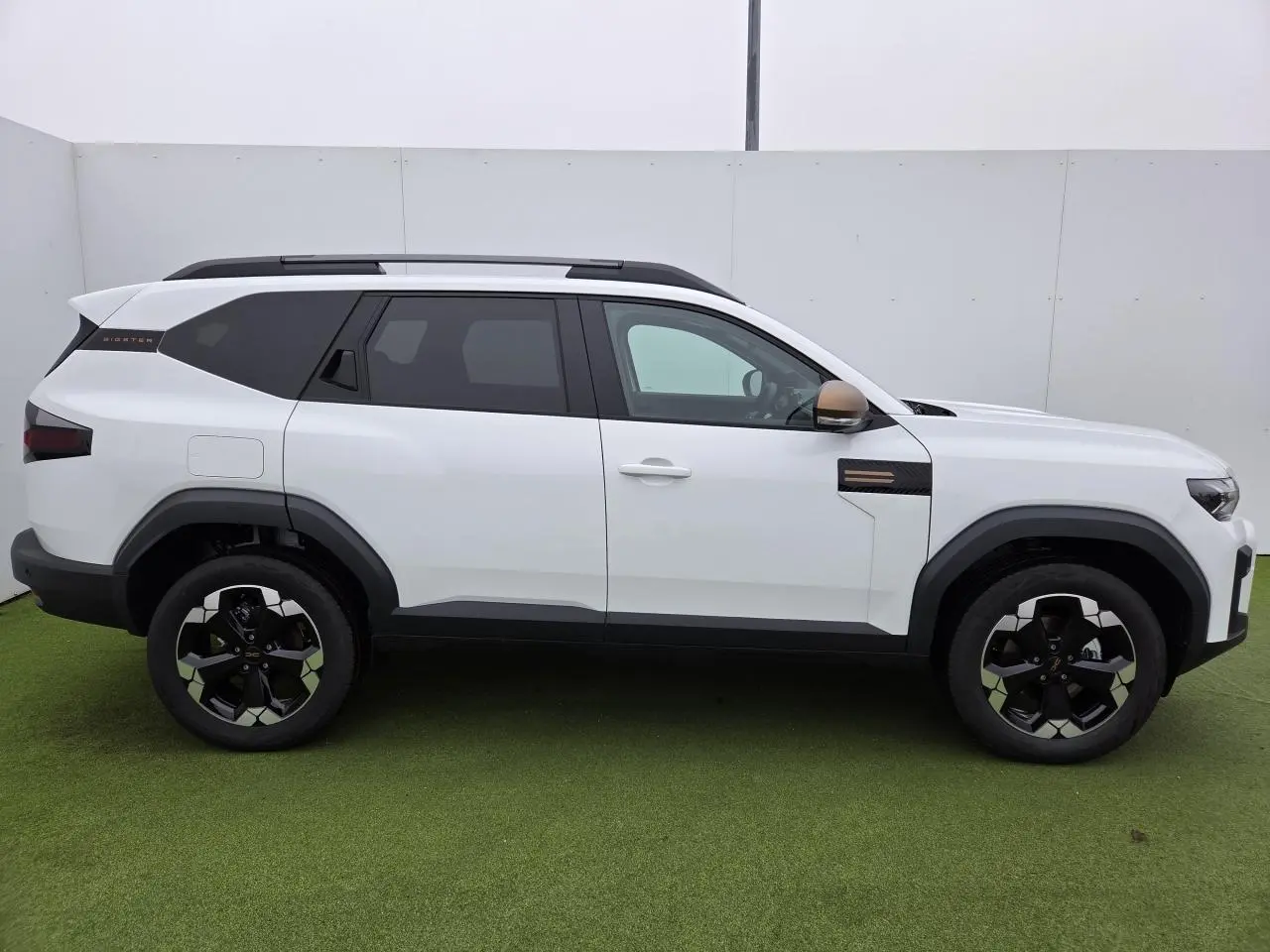 Profil côté gauche du Dacia Bigster blanc glacier avec rétroviseurs brun cuivré et jantes alliage noires.