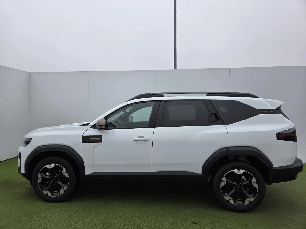 Profil côté gauche du Dacia Bigster blanc glacier 2025 avec jantes 18'' semi-diamantées et rétroviseurs brun cuivré.