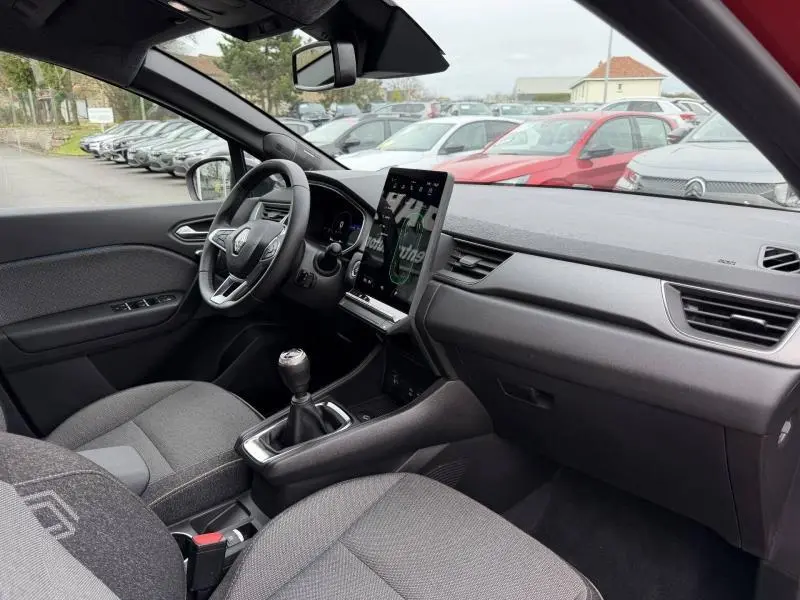 Vue intérieure côté conducteur du Renault Captur 2025 rouge, montrant le volant, la boîte manuelle et l'écran tactile vertical.
