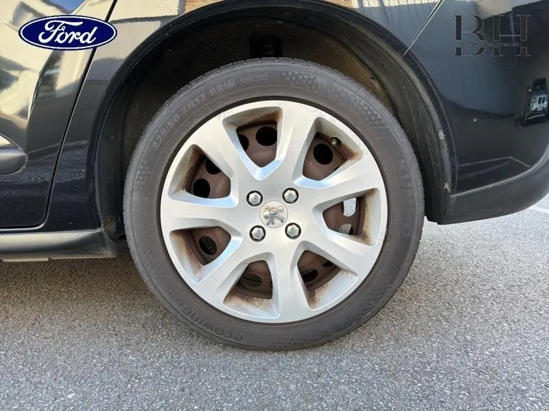 Gros plan sur la roue avant gauche d’un Peugeot 3008 noir Perla Nera avec jante alu 17 pouces et logo Peugeot central.