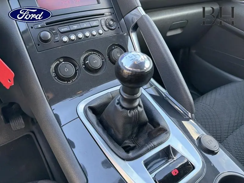 Gros plan sur la console centrale avec levier de vitesses manuel et frein à main dans un intérieur noir.