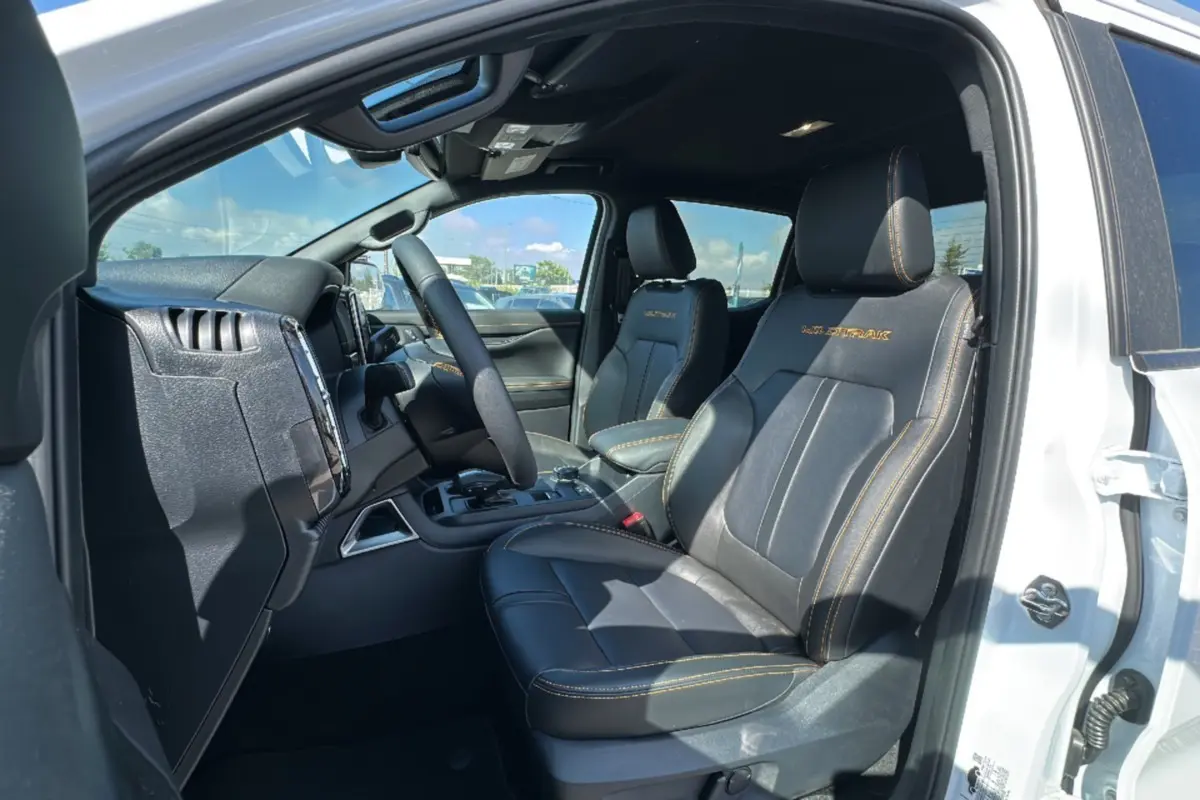 Vue intérieure côté conducteur du Ford Ranger blanc 2.3 PHEV Wildtrak avec sièges cuir noirs et surpiqûres orange.