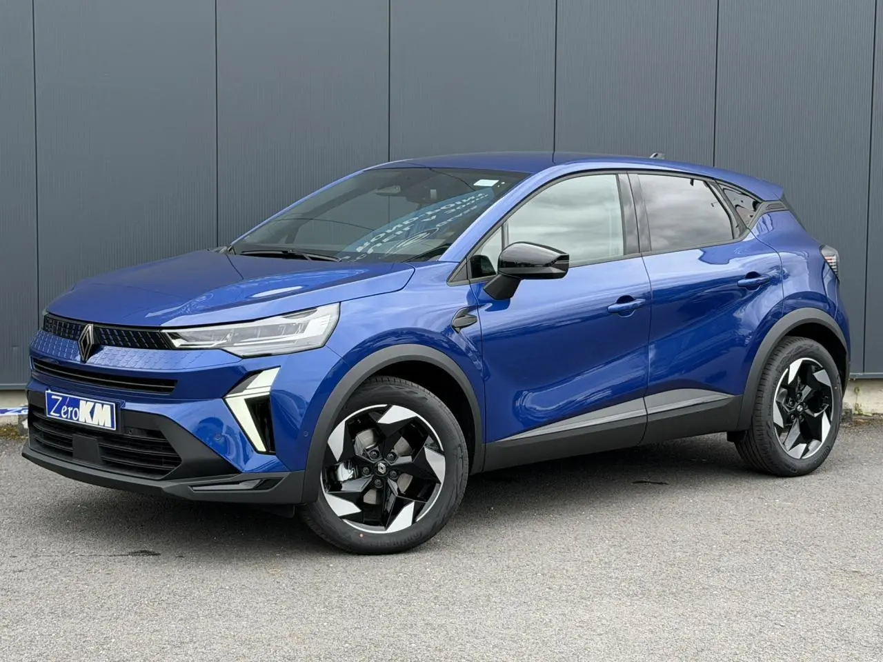 Renault Captur 2026 bleu Iron en 3/4 avant droit, avec jantes noires et détails noirs brillants sur les rétroviseurs.