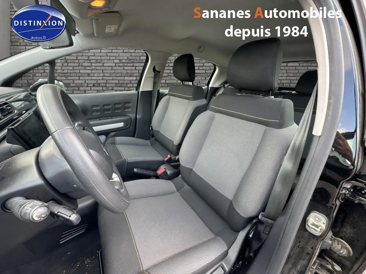 Vue intérieure côté conducteur de la Citroën C3 noire 2023, sièges tissu gris avec surpiqûres jaunes visibles.