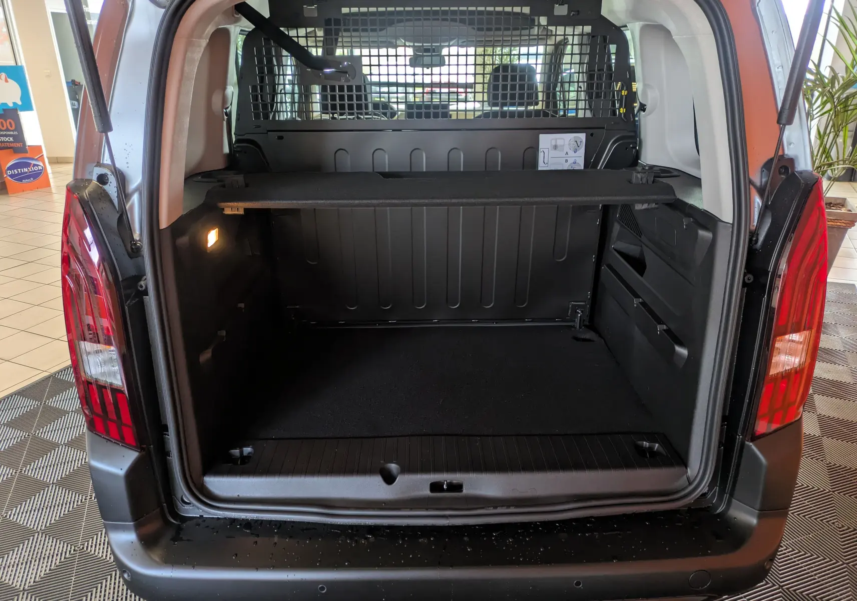 Coffre ouvert vu de l'arrière du Peugeot Rifter gris Artense 2025, avec séparation grillagée et éclairage intérieur.