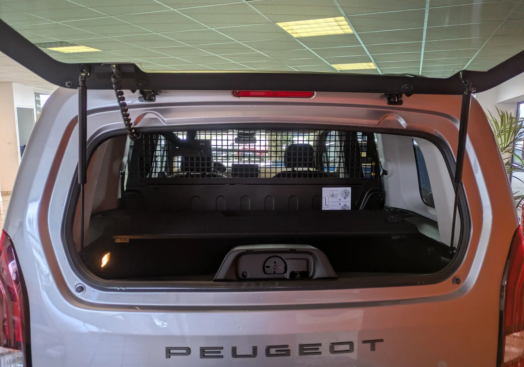 Vue arrière du Peugeot Rifter gris Artense 2025 avec hayon ouvert, montrant l’espace de chargement et la grille de séparation.