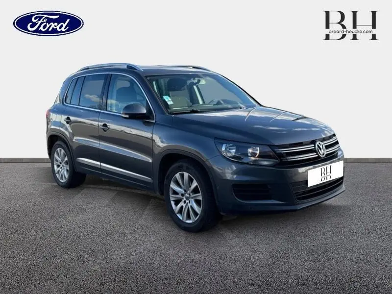 Volkswagen Tiguan 2016 gris Crypton en vue 3/4 avant droit avec jantes alu et barres de toit visibles.