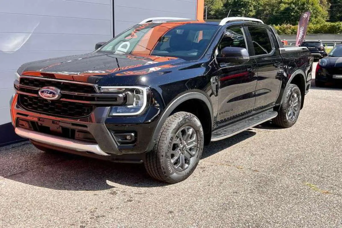 Ford Ranger 3.0 V6 Wildtrak Plus noir agate, vue 3/4 avant droit avec jantes alu et barres de toit visibles.