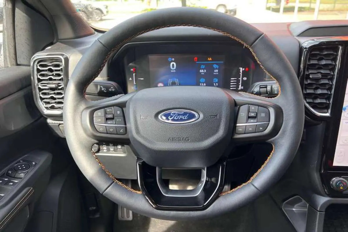 Vue rapprochée du volant cuir noir avec surpiqûres marron du Ford Ranger 2026, tableau de bord numérique visible.