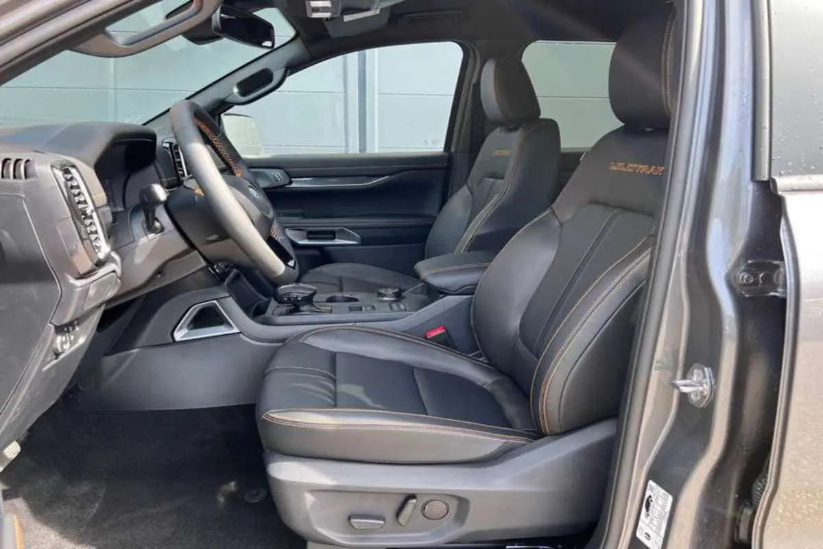 Vue intérieure côté conducteur du Ford Ranger noir agate 2026, sièges cuir Wildtrak avec surpiqûres orange visibles.