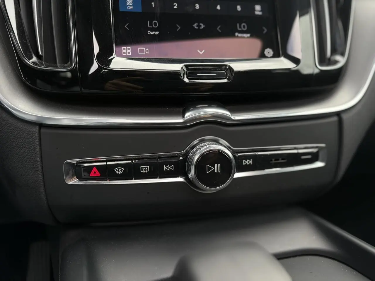 Gros plan sur la console centrale noire du Volvo XC60 2024, avec commandes multimédia et climatisation tactile.
