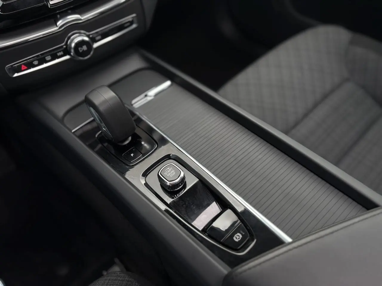 Vue rapprochée de la console centrale noire du Volvo XC60 T6 AWD PHEV 2024 avec levier de vitesse et bouton start/stop.