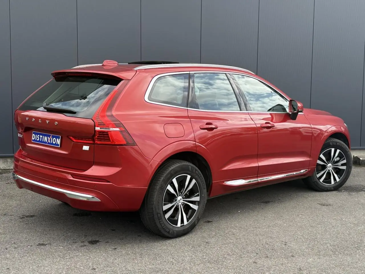 Vue 3/4 arrière droite d'un Volvo XC60 T6 AWD PHEV 2024 rouge Fusion avec jantes alliage et contour chromé.