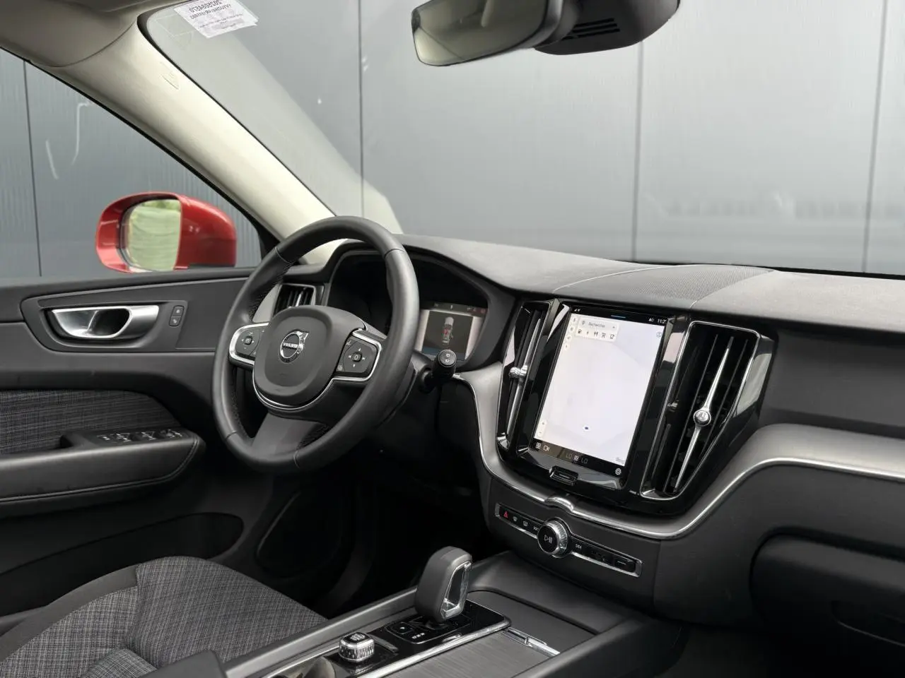 Vue intérieure côté conducteur du Volvo XC60 rouge Fusion 2024, avec tableau de bord digital et écran tactile vertical.