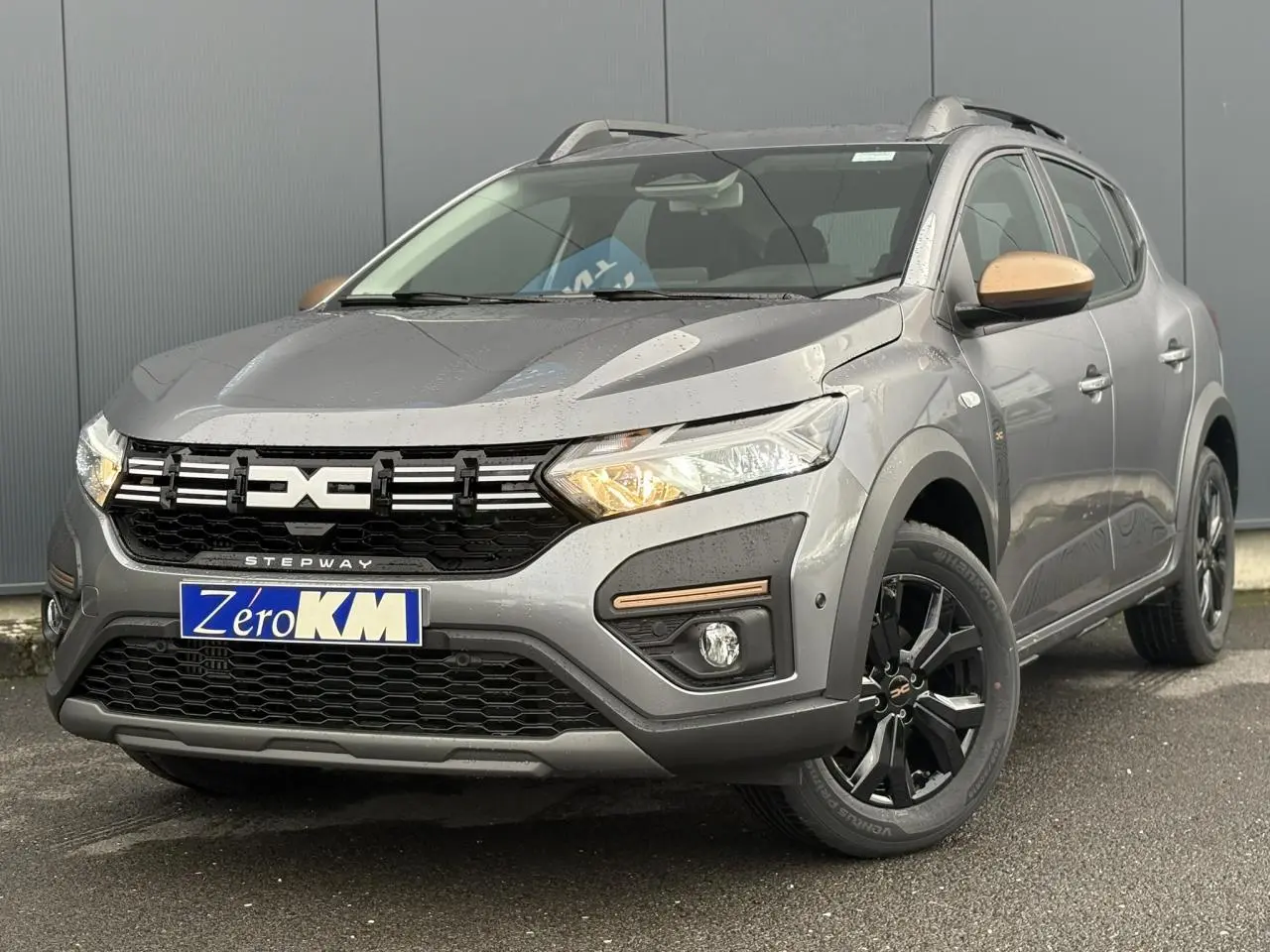 Dacia Sandero Stepway gris schiste en 3/4 avant droit avec jantes noires et coques de rétroviseurs bronze.