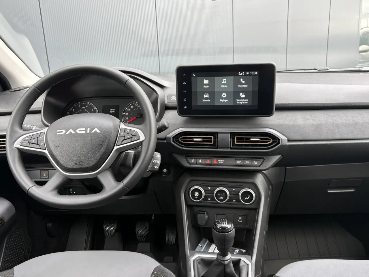 Vue intérieure frontale du tableau de bord et volant Dacia Sandero Stepway 2025, avec écran tactile et levier de vitesses manuel.