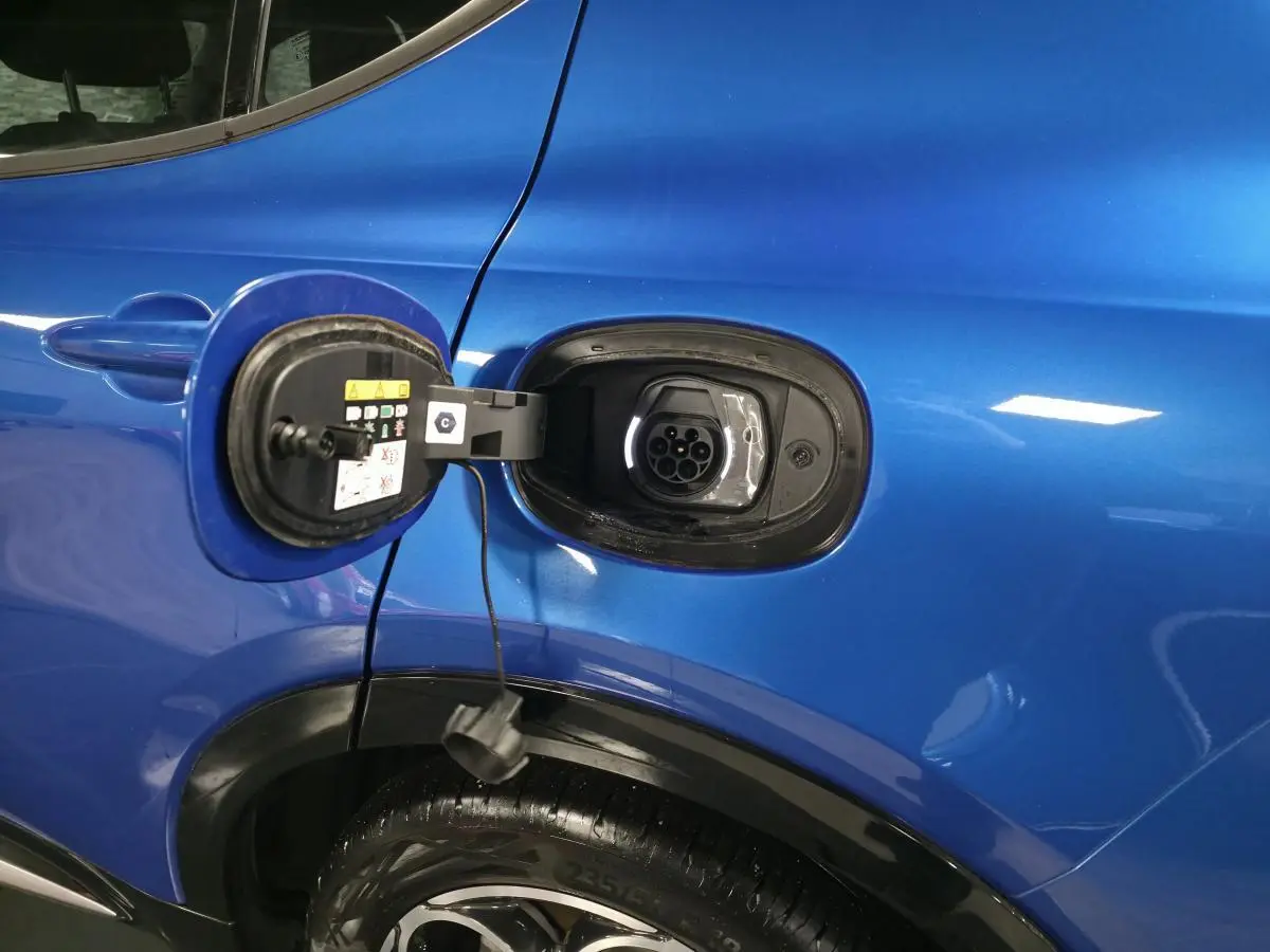 Prise de recharge ouverte côté gauche d’un Alfa Romeo Tonale bleu métallisé, avec jante alliage visible.