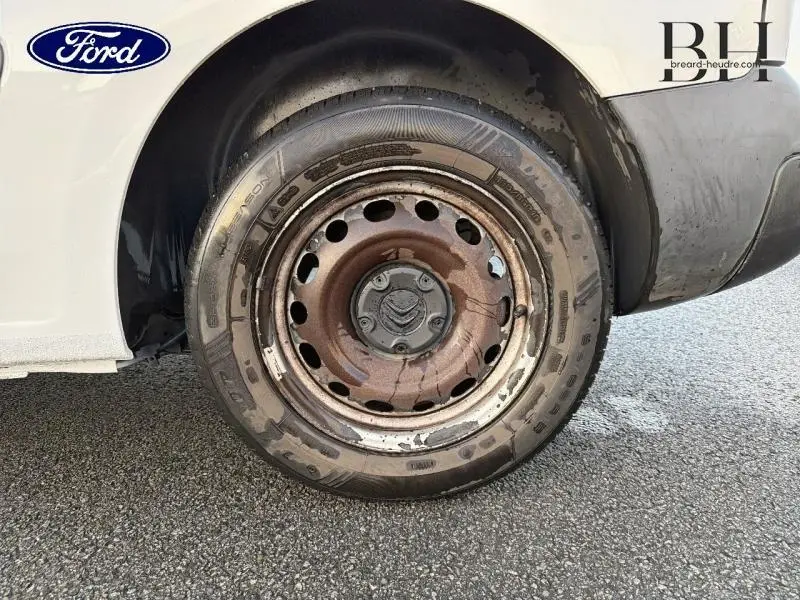 Gros plan sur la roue arrière droite rouillée d'un Citroën Berlingo blanc, avec jante acier et carrosserie partiellement visible.