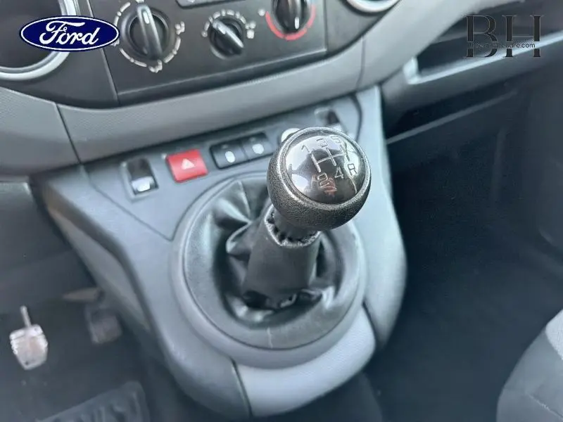 Gros plan sur le levier de vitesses manuel noir du Citroën Berlingo blanc, avec tableau de bord et commandes en arrière-plan.