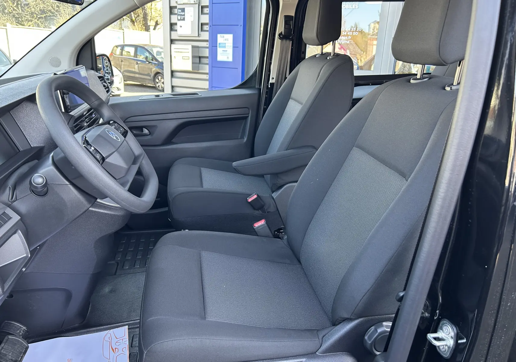 Vue intérieure côté conducteur du Citroën Jumpy Cabine Approfondie noir, montrant les sièges tissu gris et le volant.