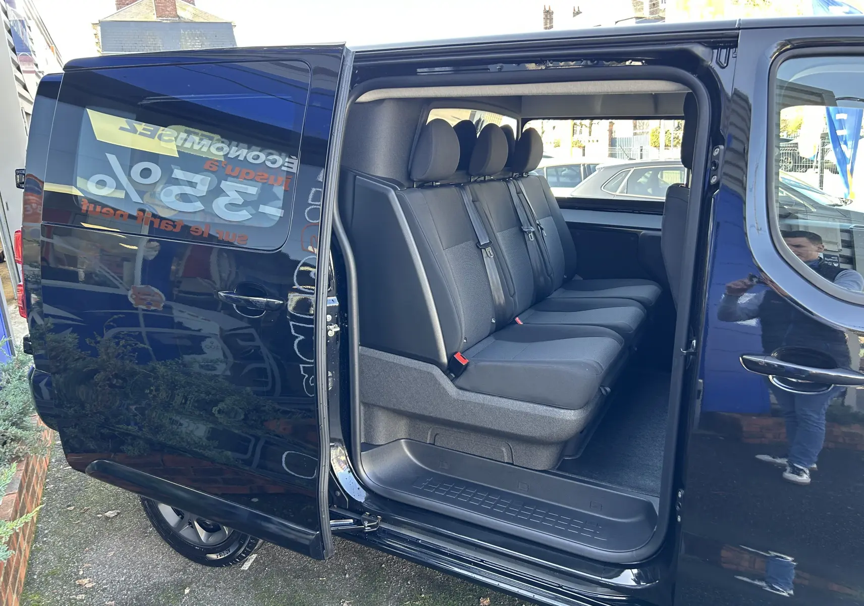Vue latérale gauche d’un Citroën Jumpy noir avec porte coulissante ouverte révélant la banquette arrière 3 places en tissu.