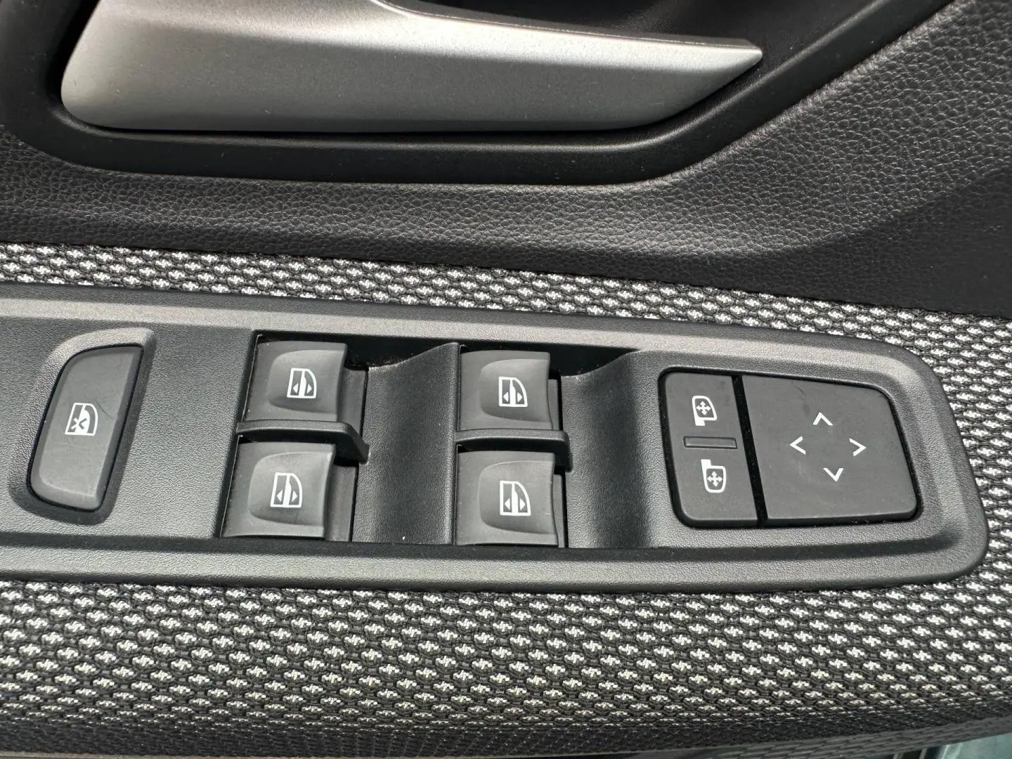 Gros plan sur les commandes des vitres électriques et réglages des rétroviseurs sur la porte côté conducteur du Dacia Jogger Vert Cèdre.