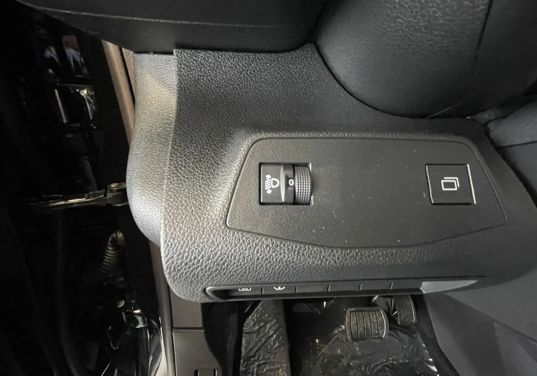 Détail du tableau de bord côté gauche du Citroën Berlingo noir 2025, avec réglage des phares et bouton de commande.
