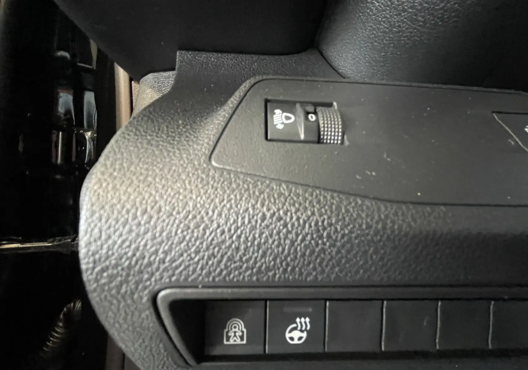 Gros plan sur les commandes de réglage des phares et du volant chauffant dans le Citroën Berlingo noir 2025.