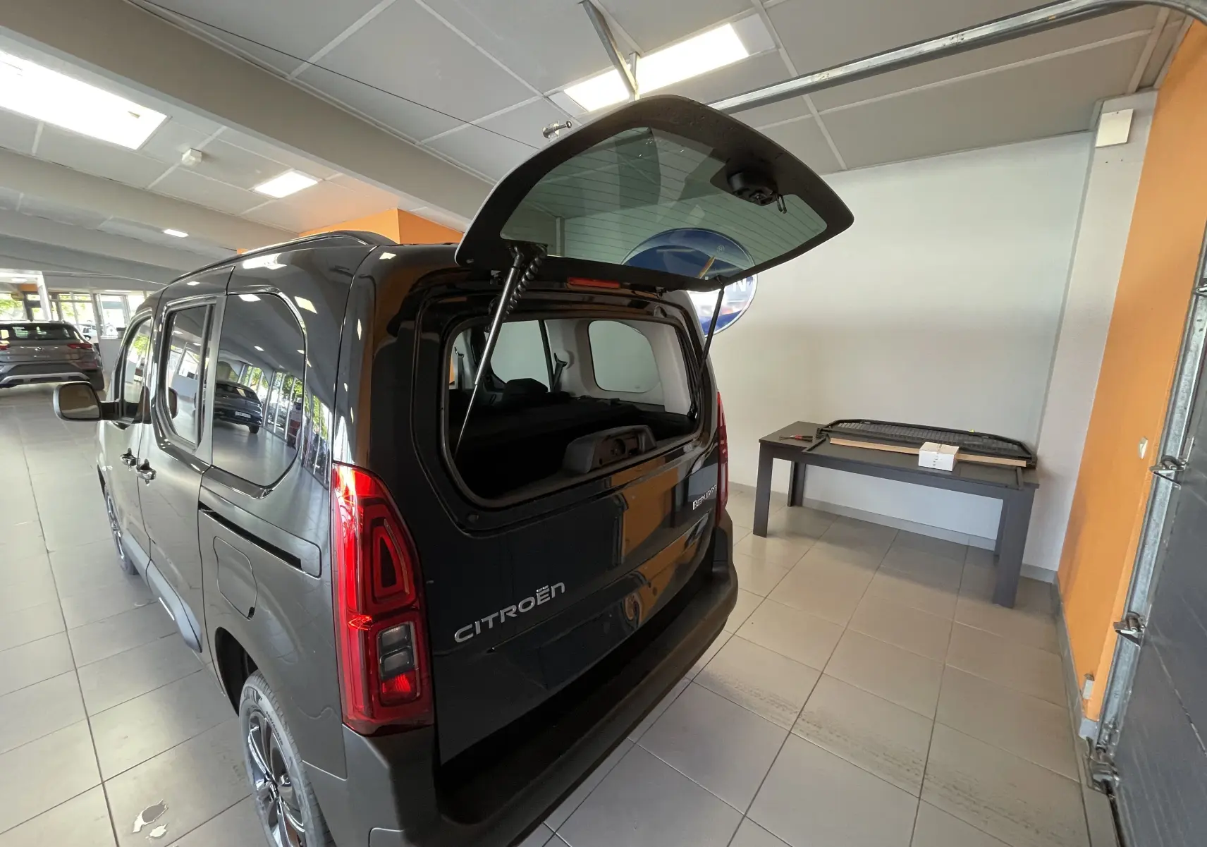 Vue 3/4 arrière droite du Citroën Berlingo noir 2025 avec hayon et lunette arrière ouverts en intérieur showroom.
