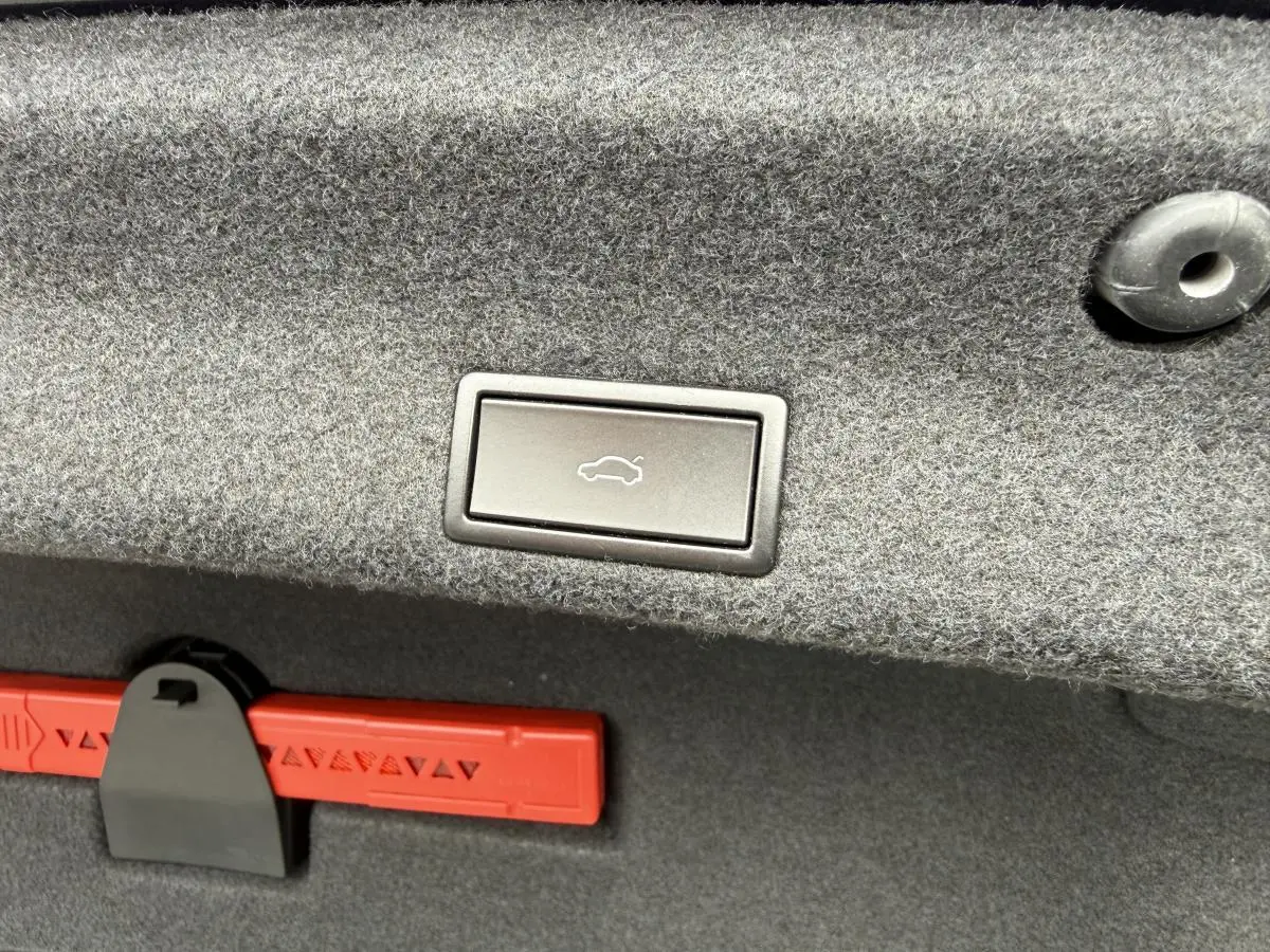 Bouton d'ouverture électrique du coffre sur la garniture grise du coffre d'une Volkswagen Passat noire 2018.