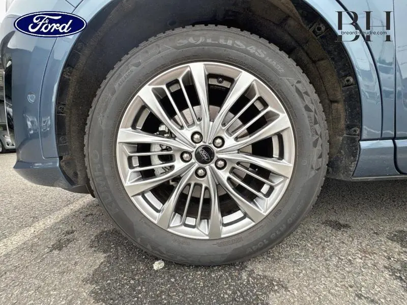 Gros plan sur la roue avant gauche en jante alu du Ford Kuga Bleu Azur Métallisée 2022 avec logo Ford au centre.