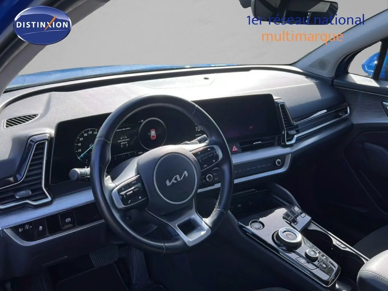 Vue intérieure du poste de conduite du Kia Sportage bleu fusion métal 2022, avec volant cuir multifonction et écran digital large.