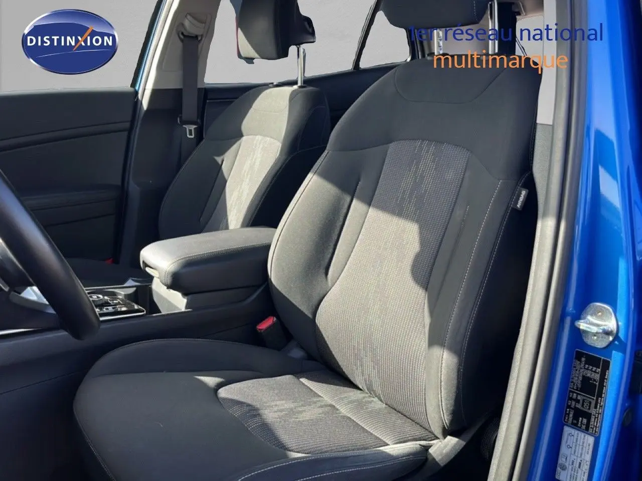 Vue intérieure côté avant droit du Kia Sportage bleu fusion métal 2022, mettant en valeur les sièges tissu noirs et l'accoudoir central.