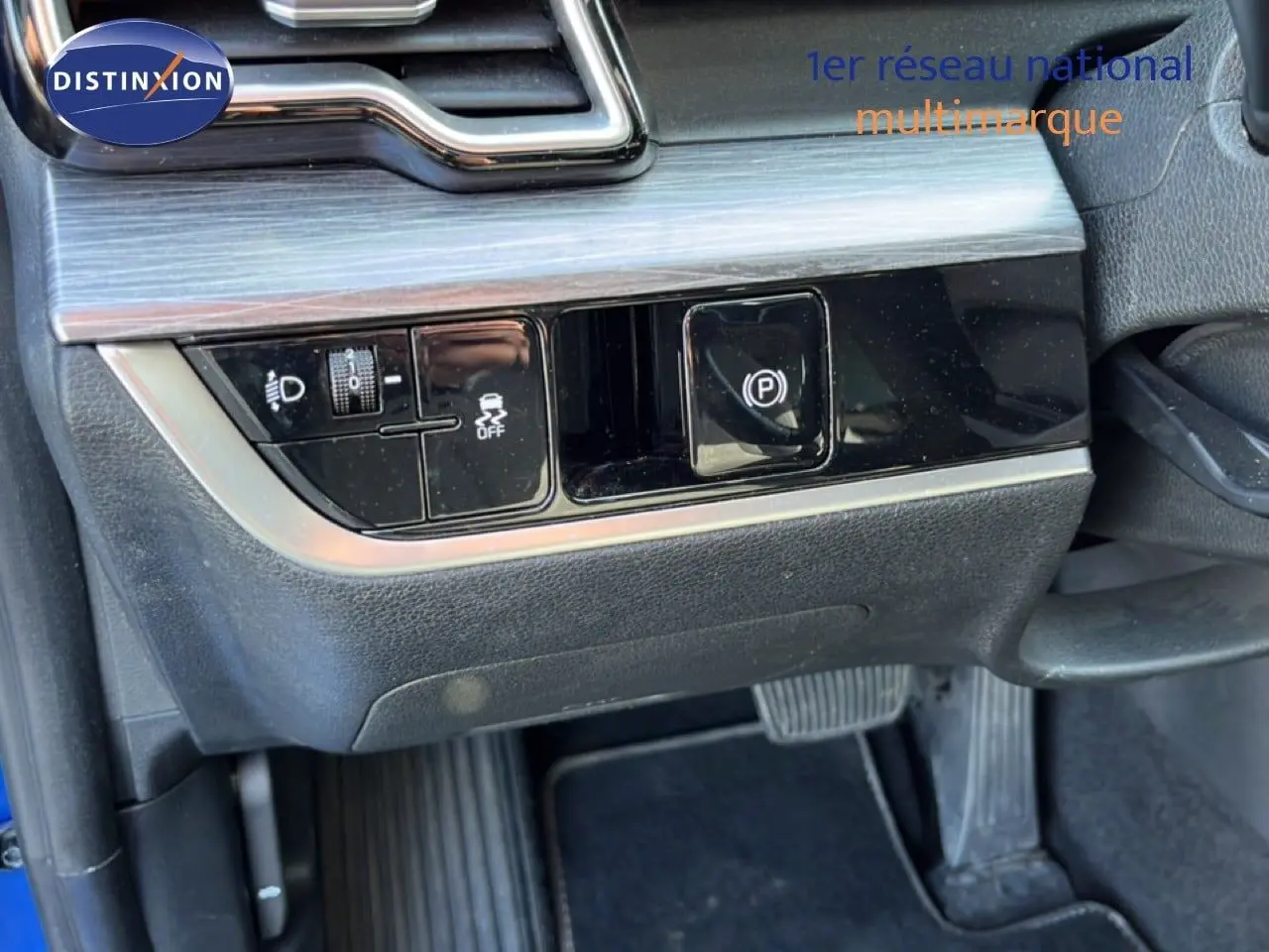Détail du tableau de bord côté gauche du Kia Sportage bleu fusion métal 2022, montrant les commandes d’éclairage et frein à main électrique.