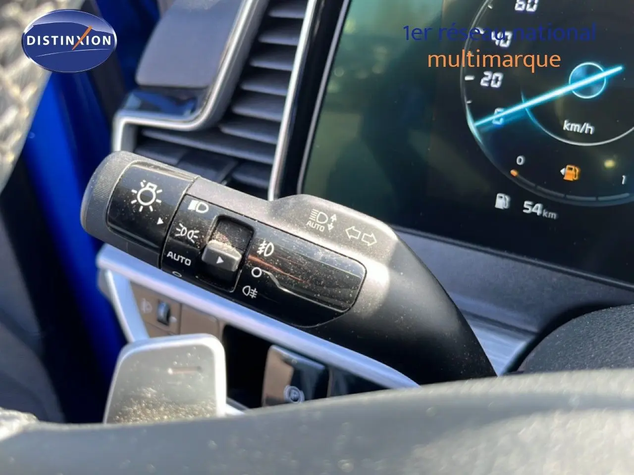 Gros plan sur la commande des feux et clignotants du Kia Sportage bleu fusion, avec tableau de bord digital affichant 54 km.