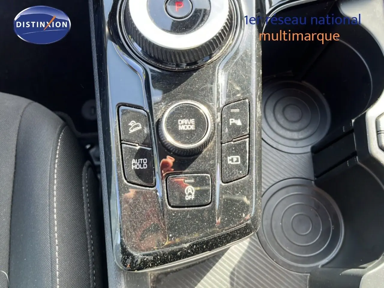 Gros plan sur la console centrale du Kia Sportage 2022, montrant les commandes de mode de conduite et maintien auto, avec porte-gobelets.