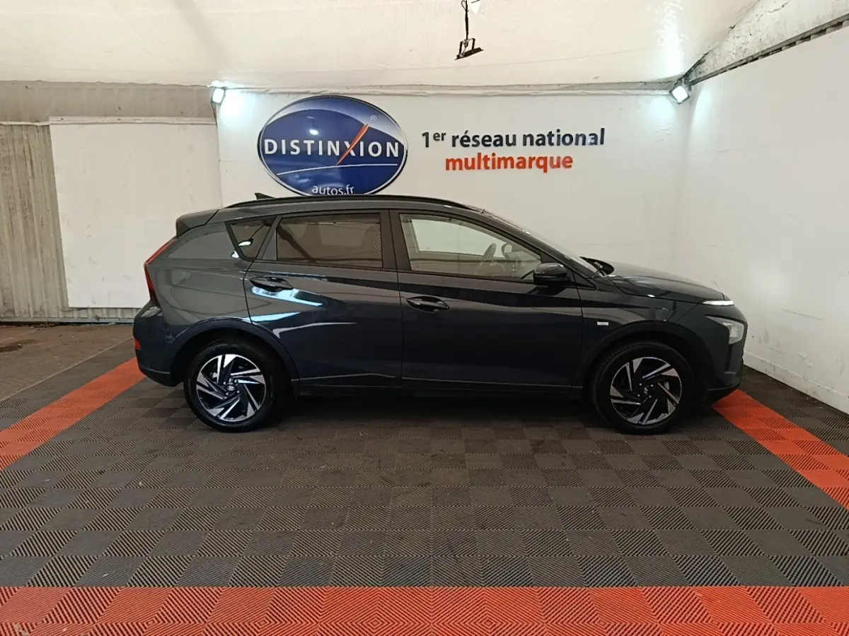 Vue latérale droite d'une Hyundai Bayon gris foncé 2023 avec jantes alliage et toit noir dans un showroom.