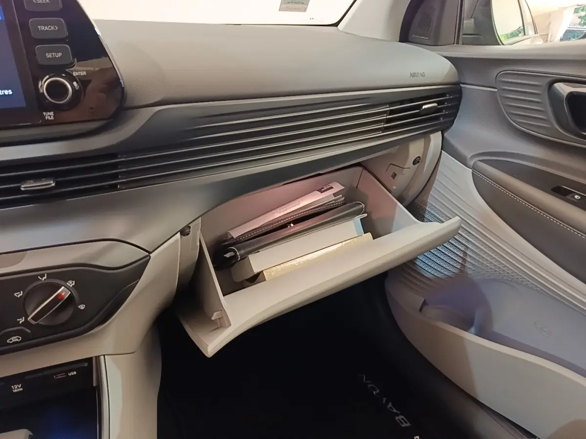 Vue intérieure côté passager du tableau de bord gris clair de la Hyundai Bayon 2023 avec boîte à gants ouverte contenant des documents.
