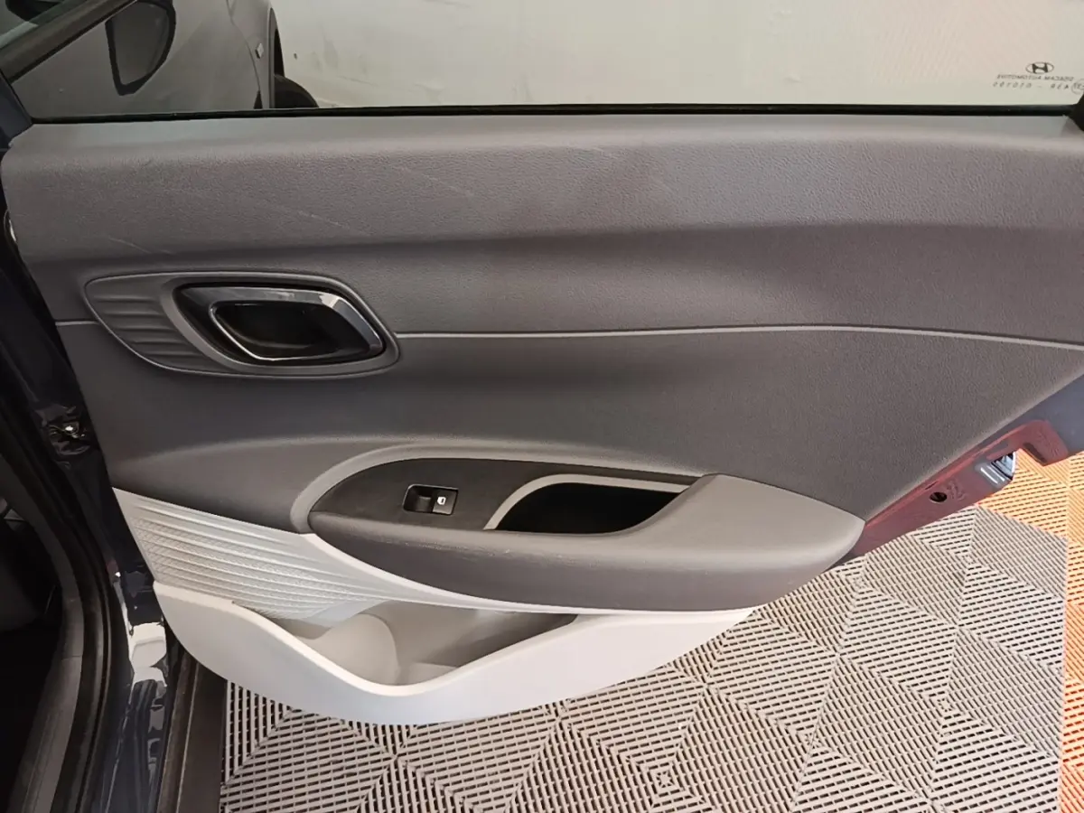 Vue rapprochée de la porte avant gauche gris foncé de la Hyundai Bayon 2023, avec poignée intérieure chromée et commande de vitre.