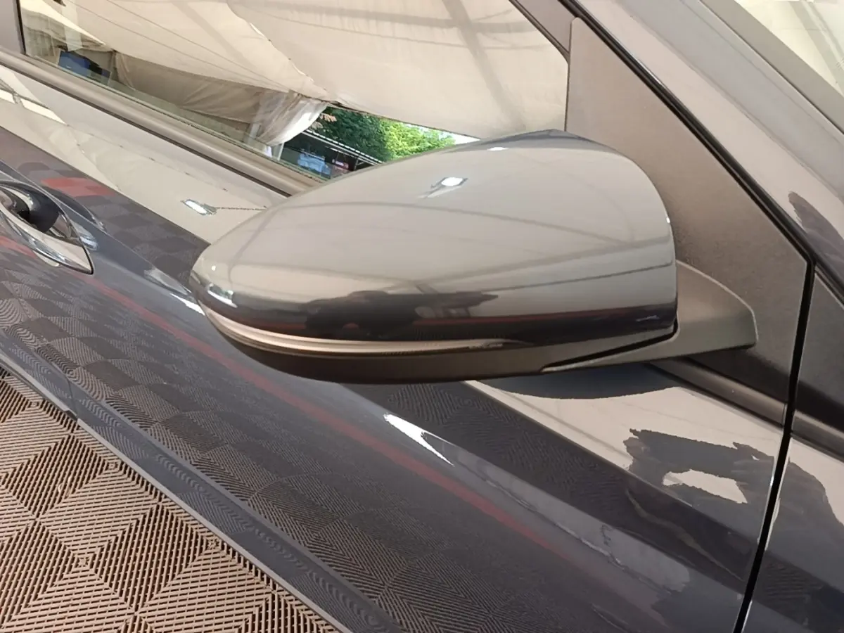 Gros plan sur le rétroviseur droit gris foncé d'une Hyundai Bayon 2023, avec reflet et poignée de porte visible.