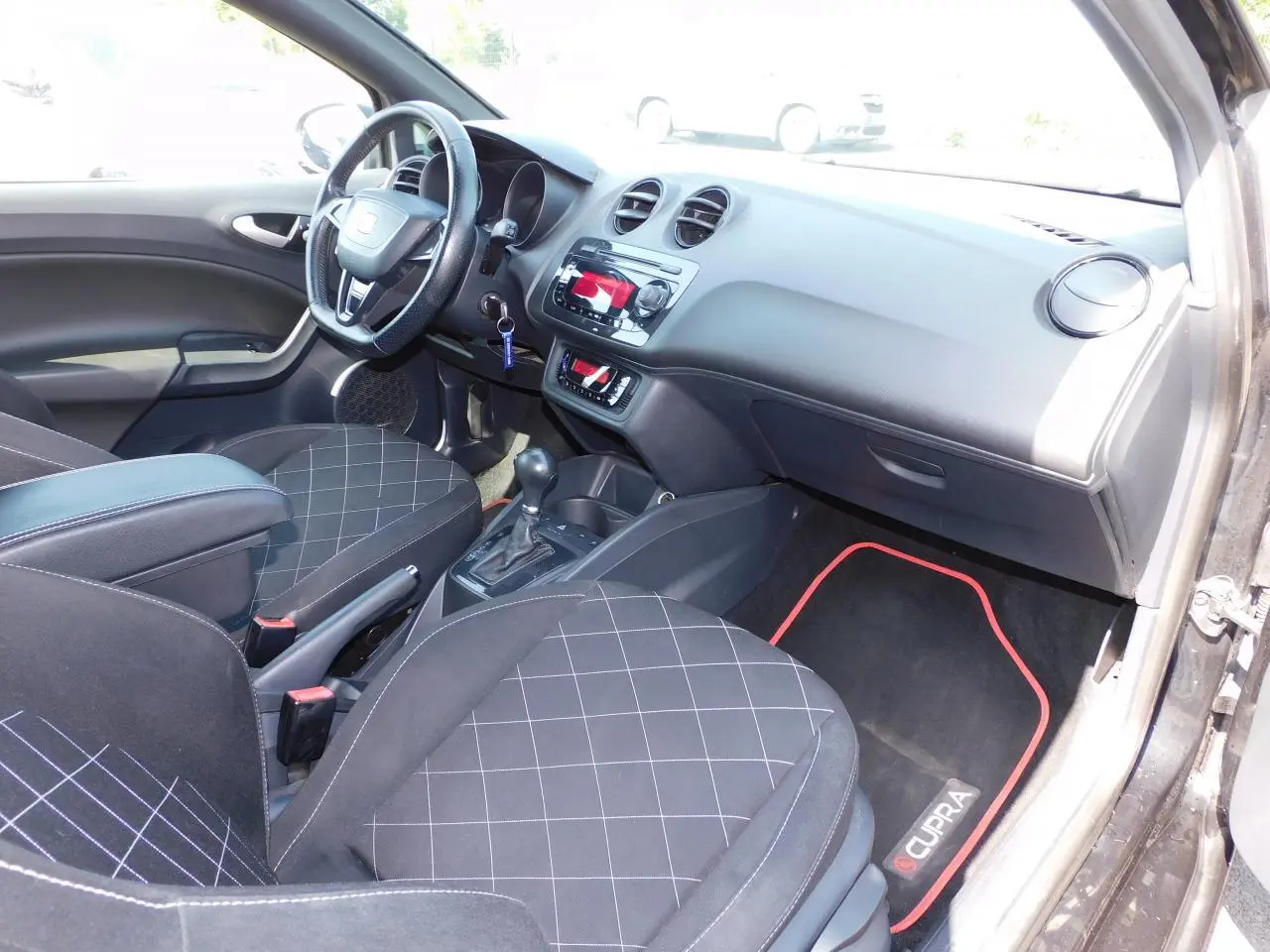 Intérieur avant droit de la SEAT Ibiza Cupra noire, sièges sport à motifs, volant cuir et tapis spécifiques Cupra rouges.