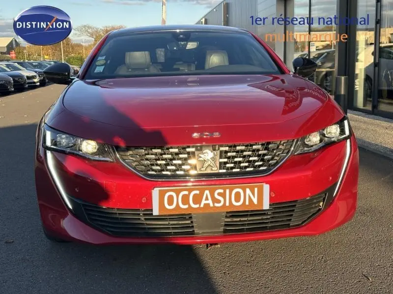 Vue frontale d'une Peugeot 508 rouge Ultimate avec calandre chromée et plaque "OCCASION" visible.