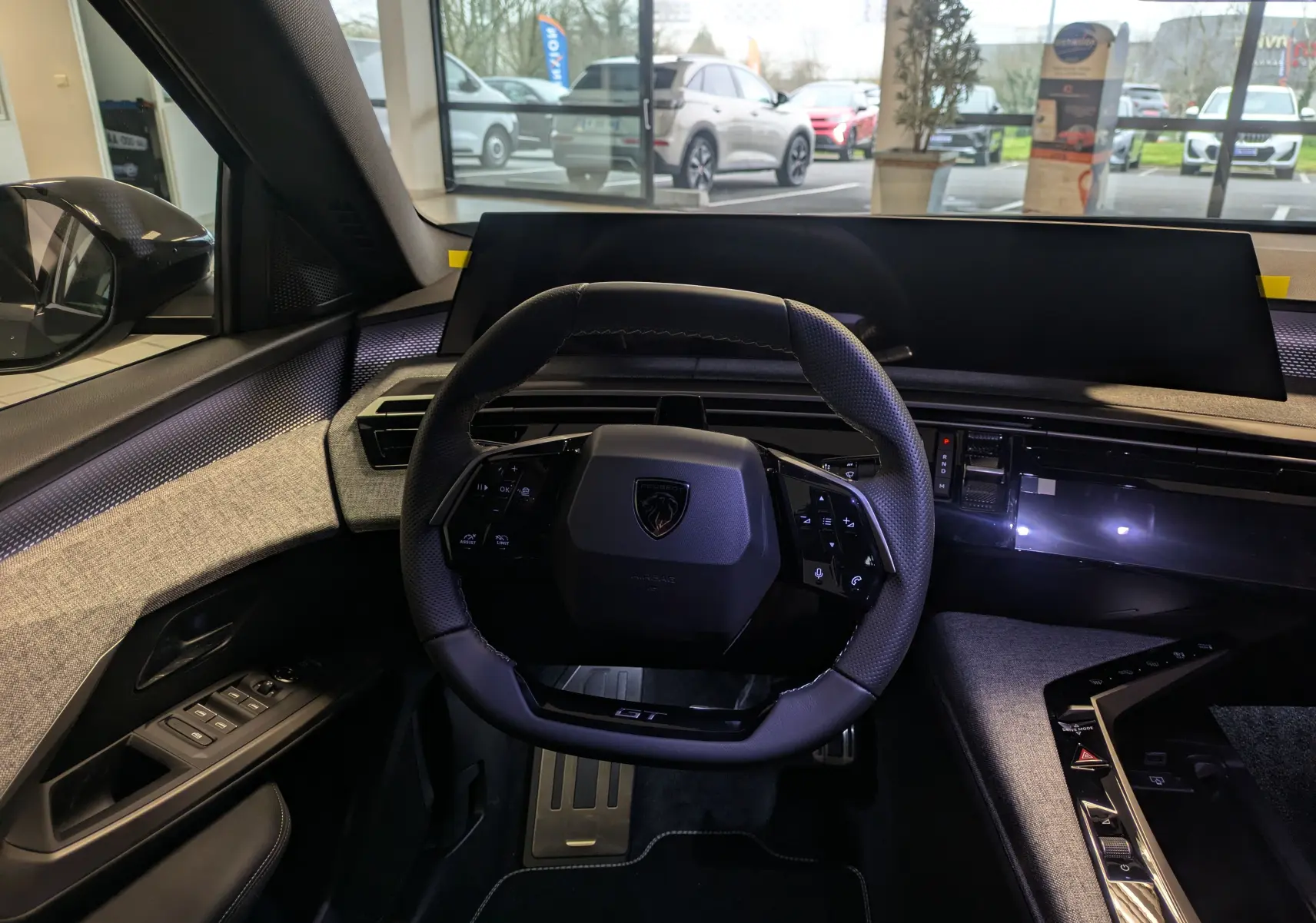 Vue intérieure centrée sur le volant compact du Peugeot 3008 gris titanium, avec tableau de bord numérique et finitions tissu grises.