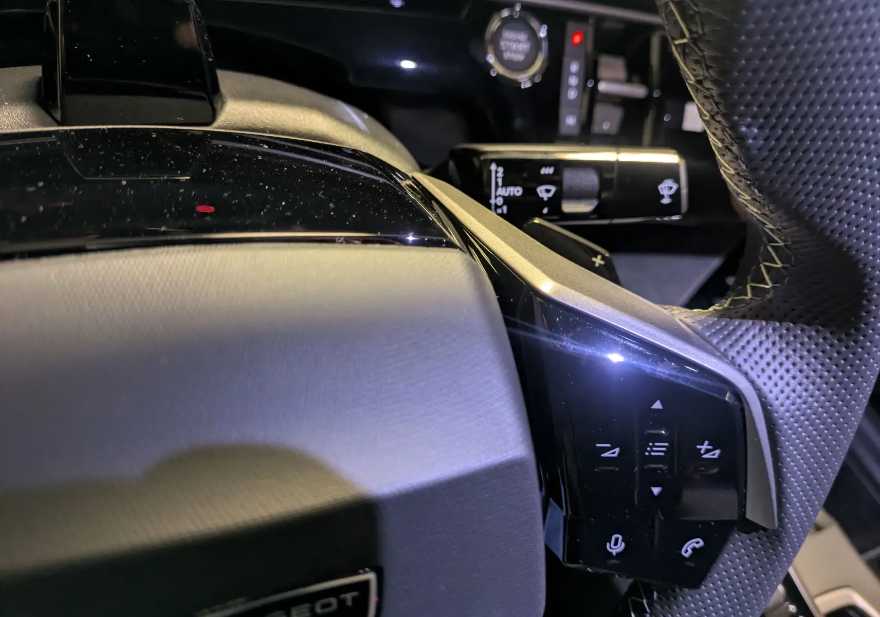 Gros plan sur la partie droite du volant perforé du Peugeot 3008 gris titanium, avec commandes intégrées et bouton start/stop visible.