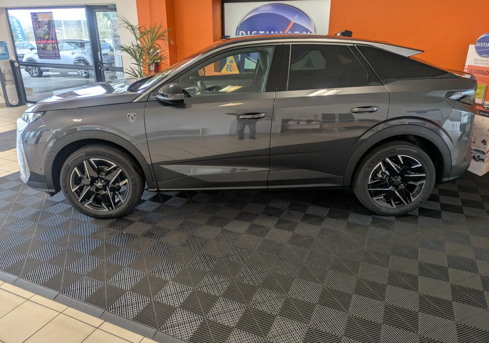 Vue de profil côté gauche d’un Peugeot 3008 gris titanium 2026 avec jantes noires et toit noir en concession.