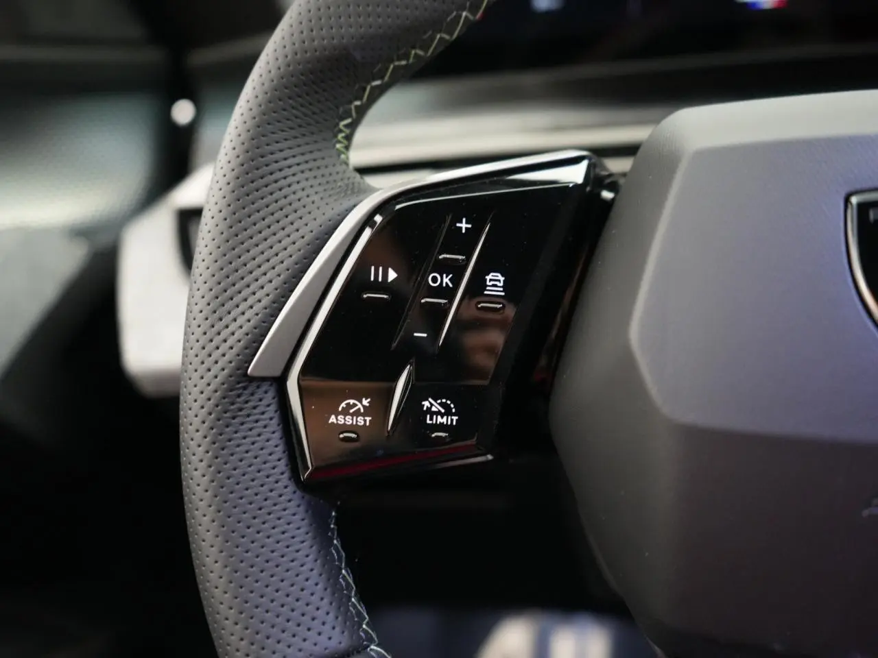 Gros plan sur les commandes gauche du volant perforé noir du Peugeot 3008 hybride 2026, avec boutons d'assistance et limiteur.