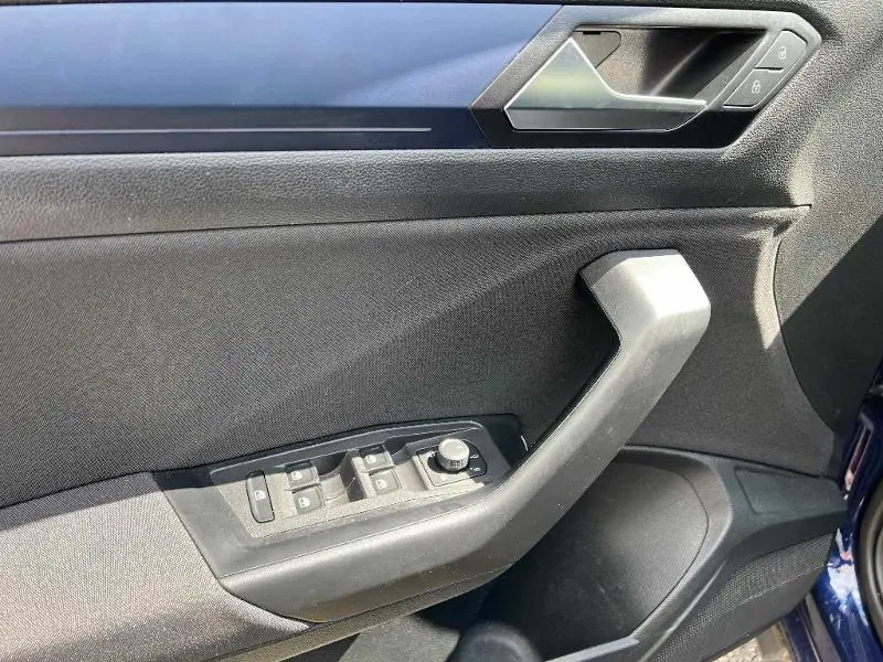 Gros plan sur la porte côté gauche du Volkswagen T-Roc gris 2020, montrant les commandes des vitres et la poignée intérieure.