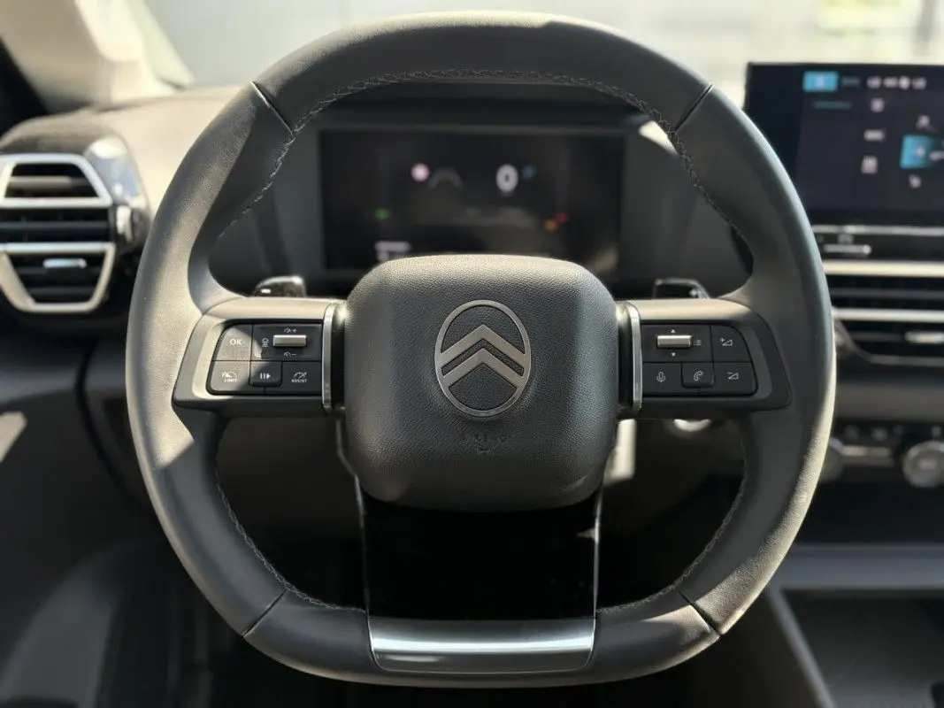Gros plan sur les commandes gauche du volant noir de la Citroën C4 Hybrid 145 CH, avec tableau de bord flou en arrière-plan.