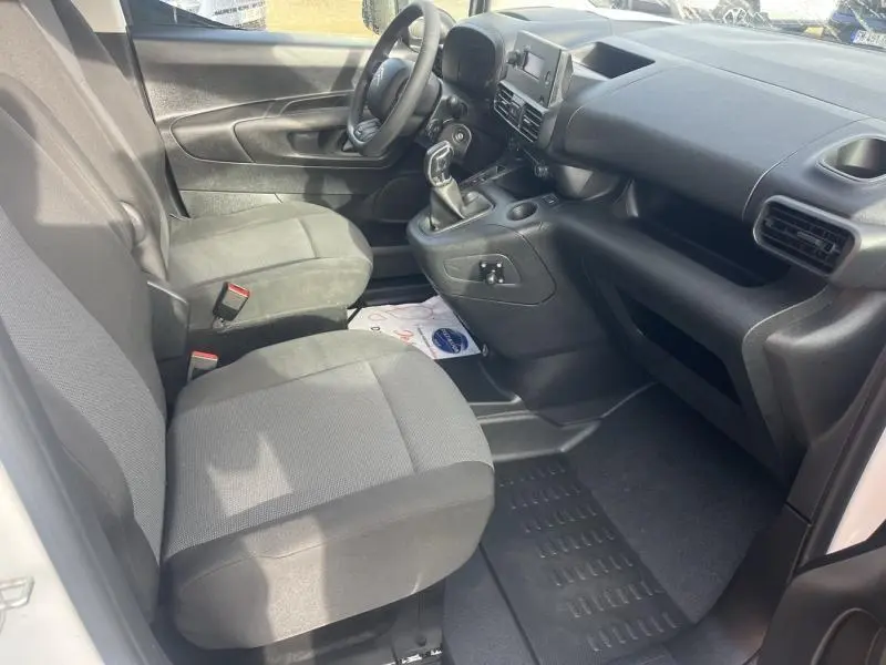 Intérieur avant du Citroën Berlingo Fourgon blanc, vue côté gauche montrant sièges tissu gris et tableau de bord noir.