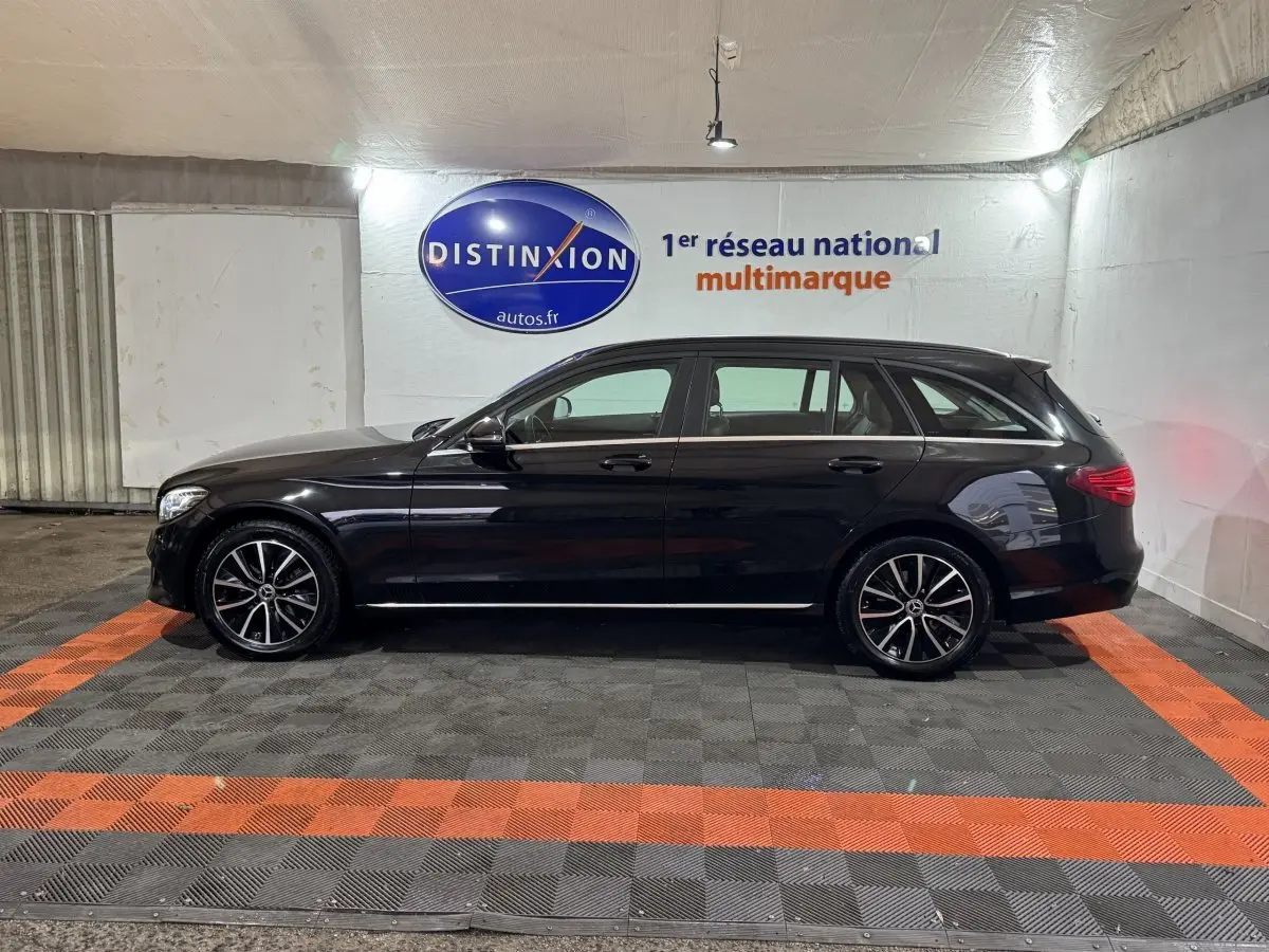 Profil côté gauche d'un break Mercedes Classe C noir 2019 avec jantes alliage et toit chromé dans un showroom.